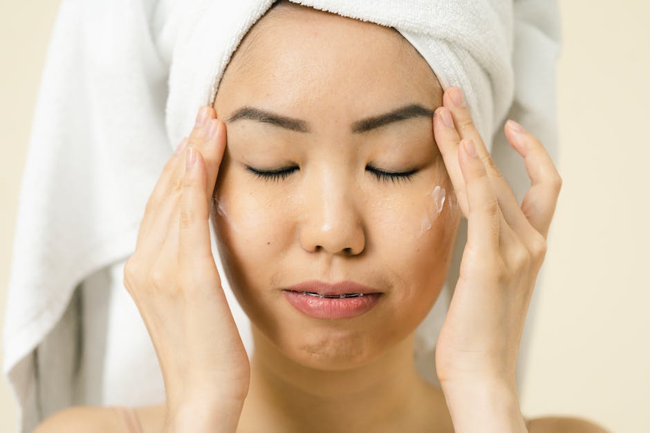 Asian woman with a towel on head applying moisturizer for skincare routine