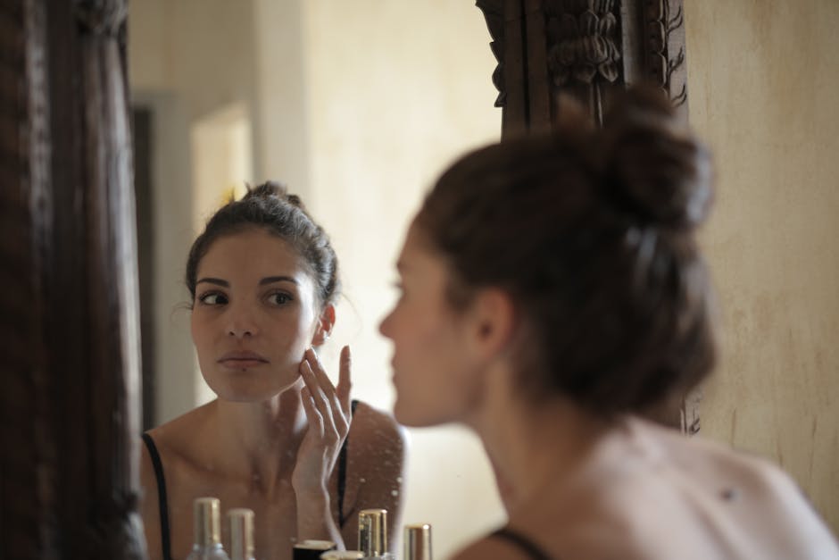 A woman checks her skin in the mirror, engaging in her morning skincare routine indoors